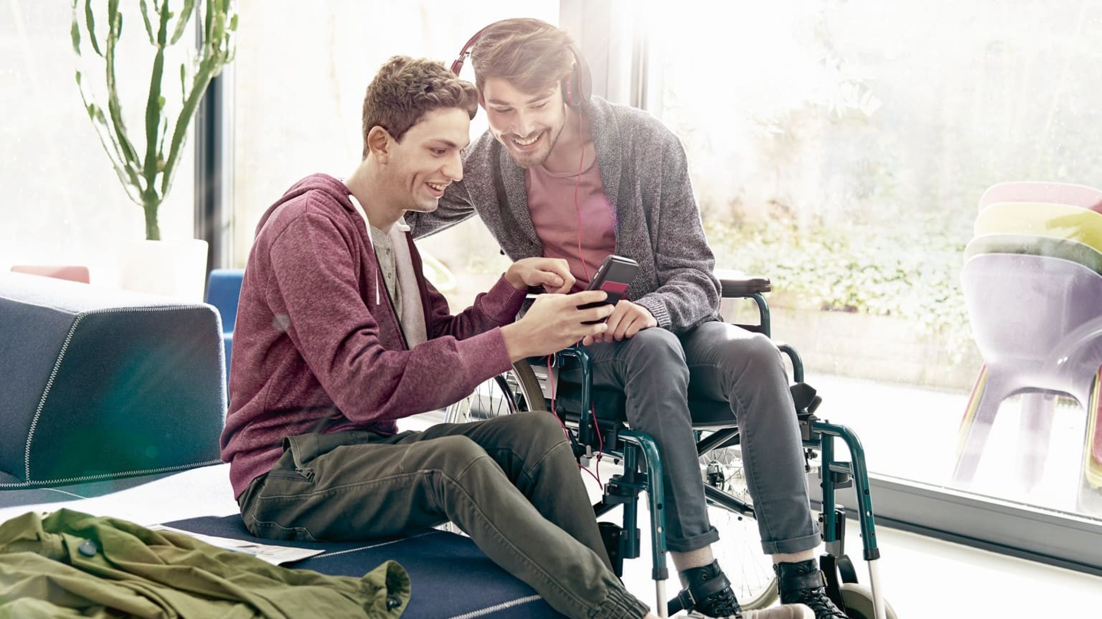 Junger Mann im Rollstuhl schaut mit Freund Film auf Handy an
