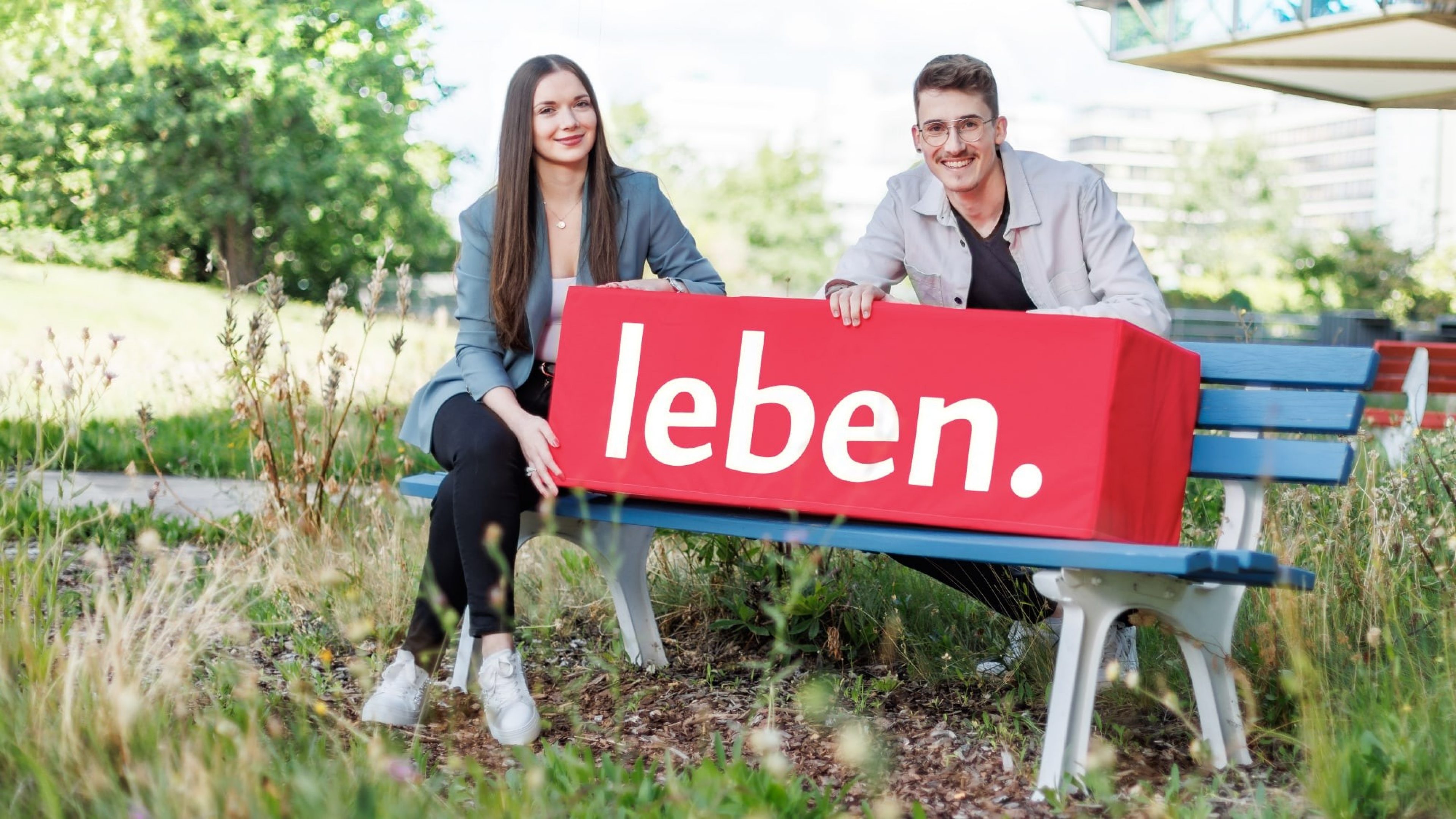 Studentin und Auszubildender von Swiss Life sitzen auf einer Bank vor der Servicezentrale