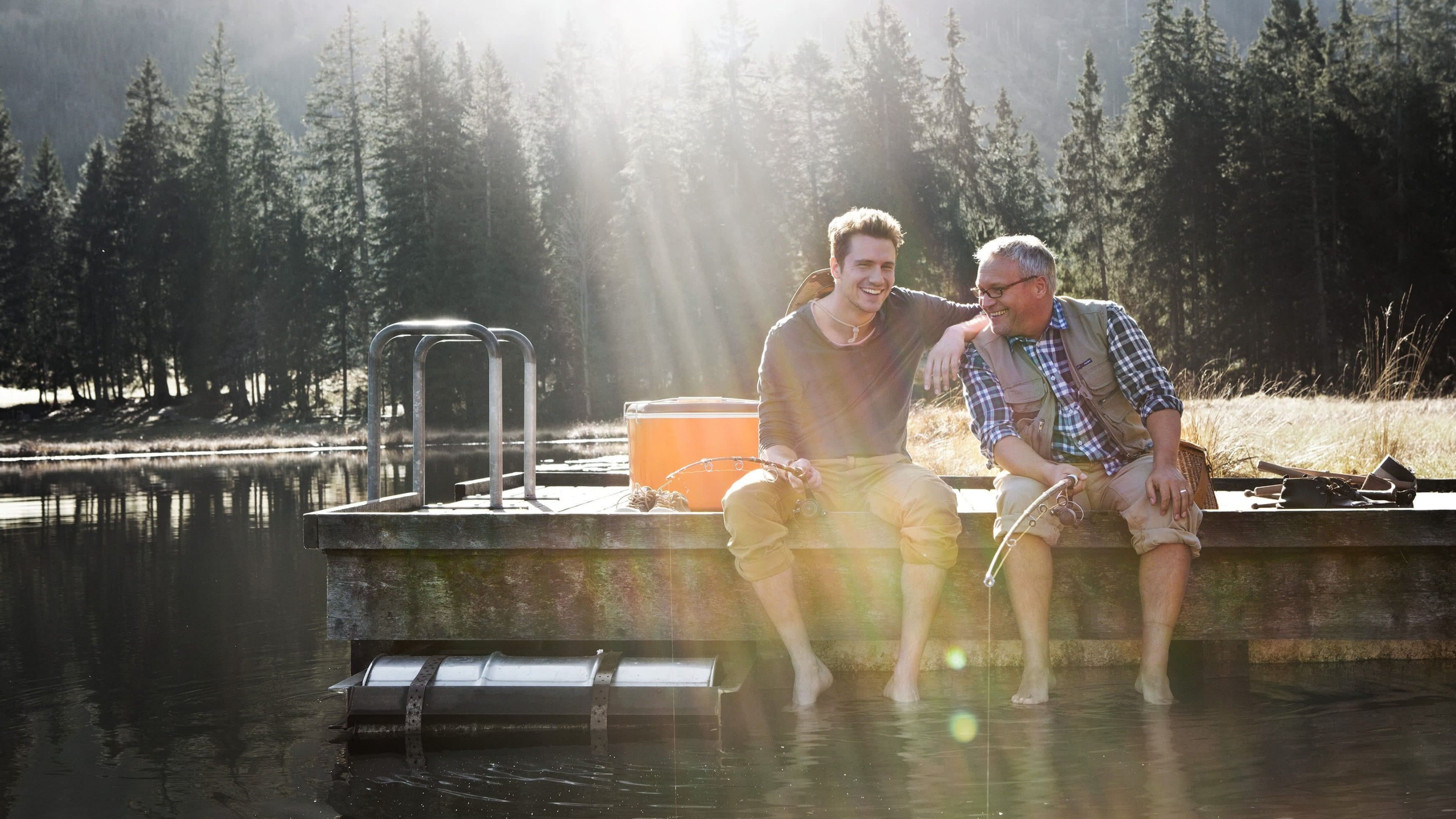 Sohn und Vater sitzen an einem Steg unterhalten sich und lassen Füße im Wasser hängen