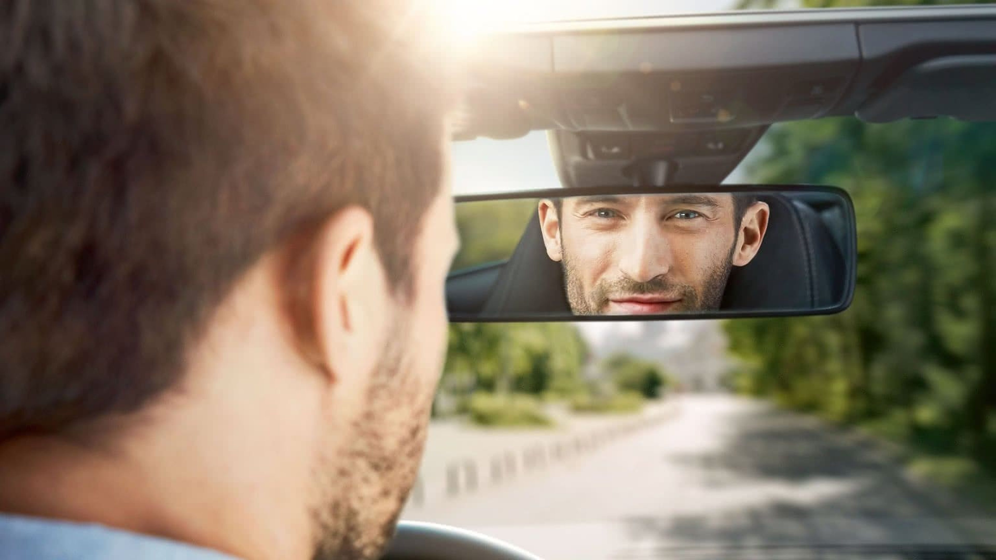 Junger Mann in blauem Hemd mit Blick in die Kamera  lehnt an einem Cabrio