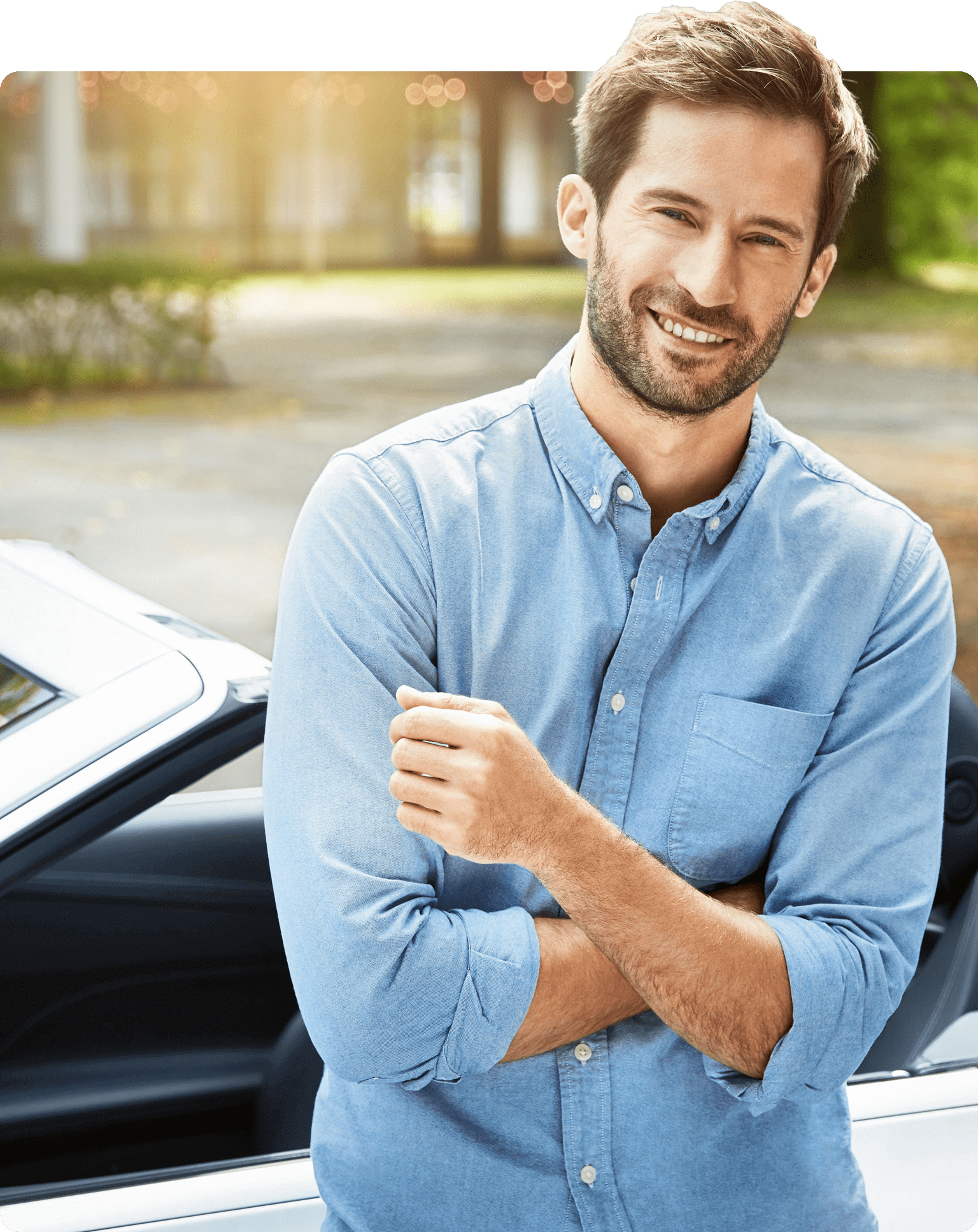 Junger Mann in blauem Hemd mit Blick in die Kamera  lehnt an einem Cabrio