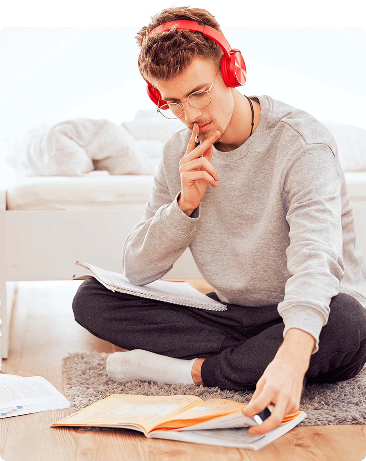 Student hört mit roten Kopfhörer Musik und sitzt am Boden und studiert Bücher
