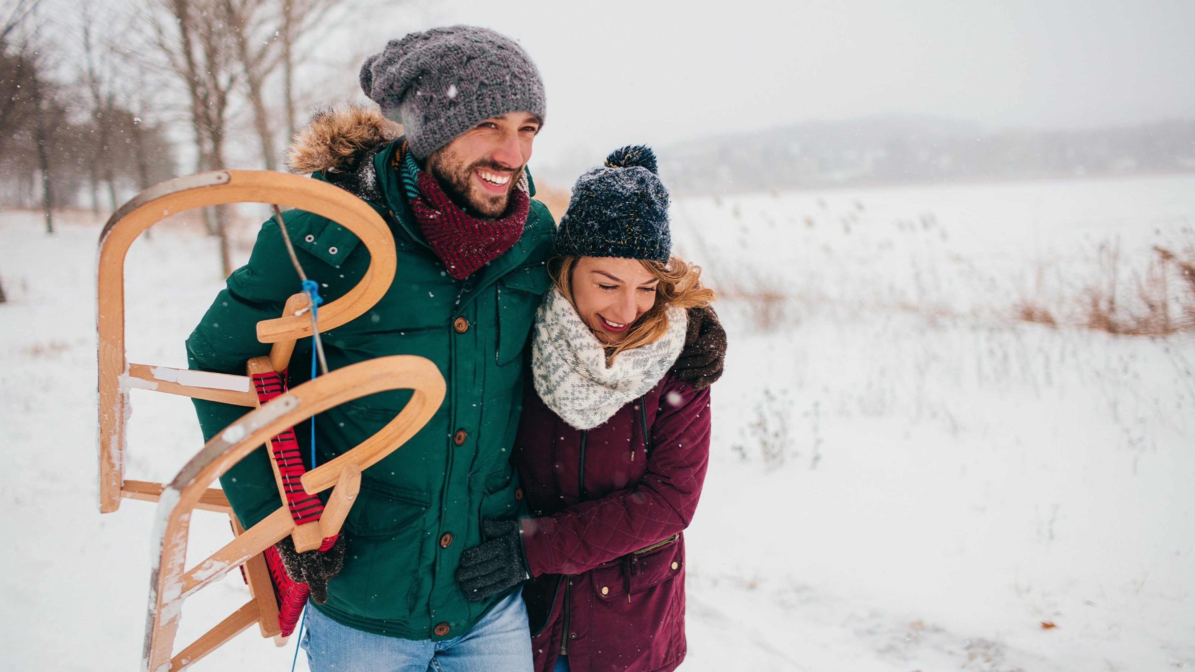 Glückliches Paar geht im Schnee spazieren, der Mann hat einen Schlitten in der Hand