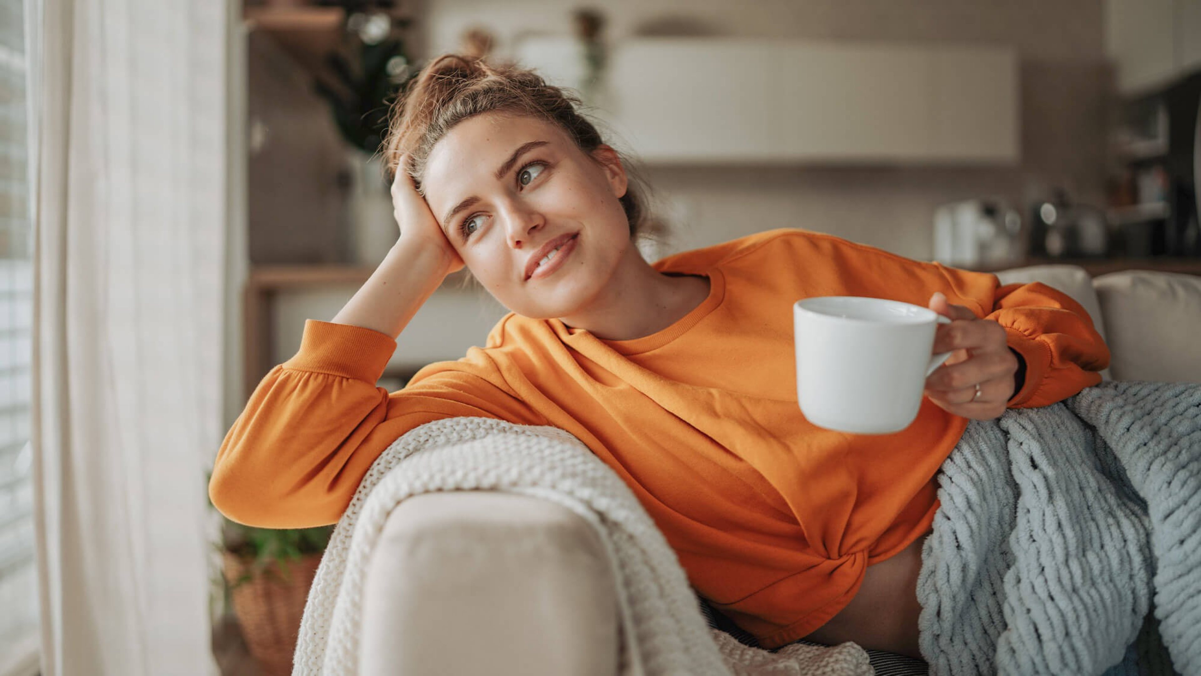 Junge Frau entspannt auf Sofa mit Kaffeetasse