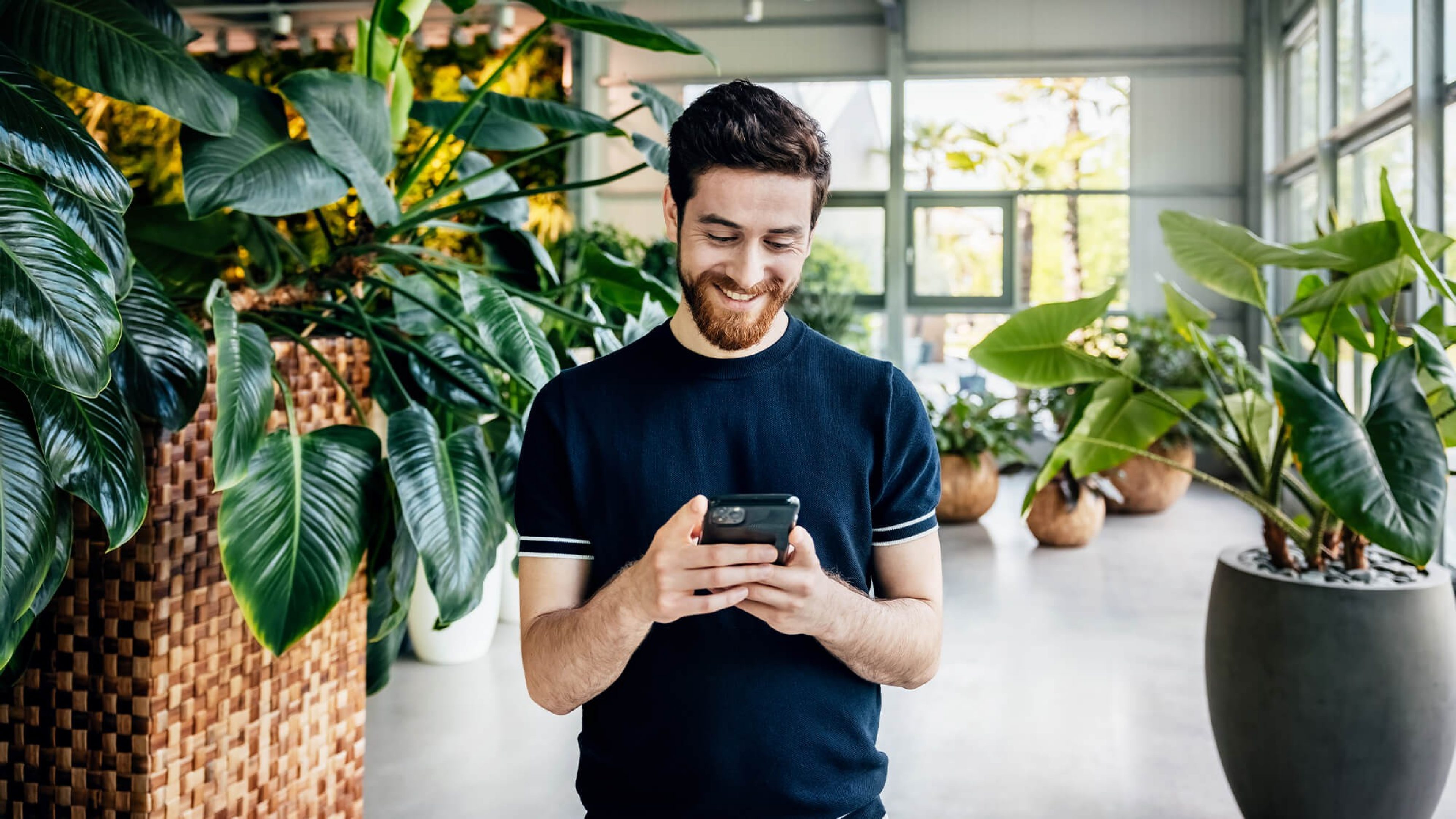 Mann mit Smartphone in Büro mit vielen Pflanzen