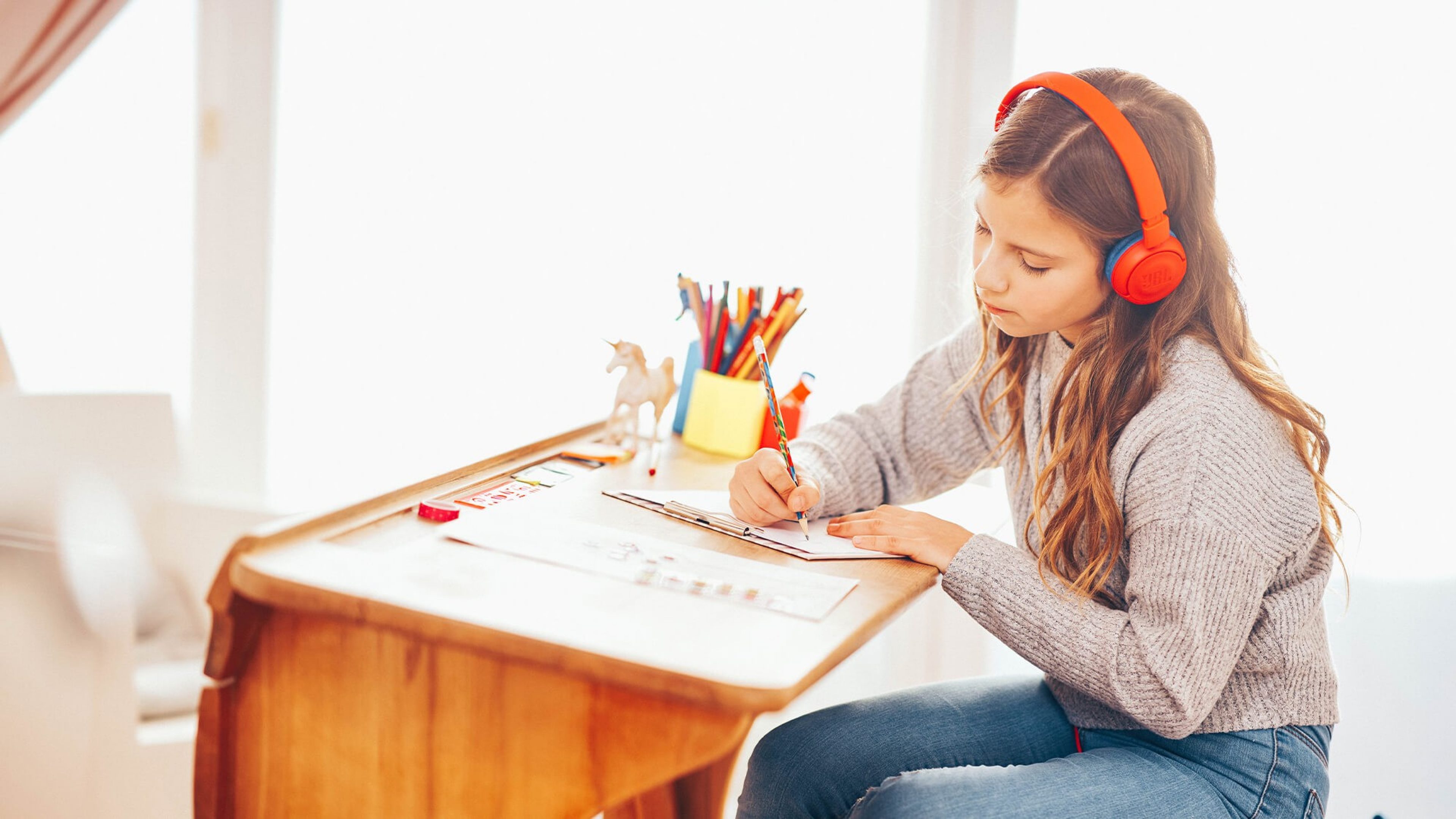 Mädchen mit Kopfhörern an Schreibtisch mit Hausaufgaben