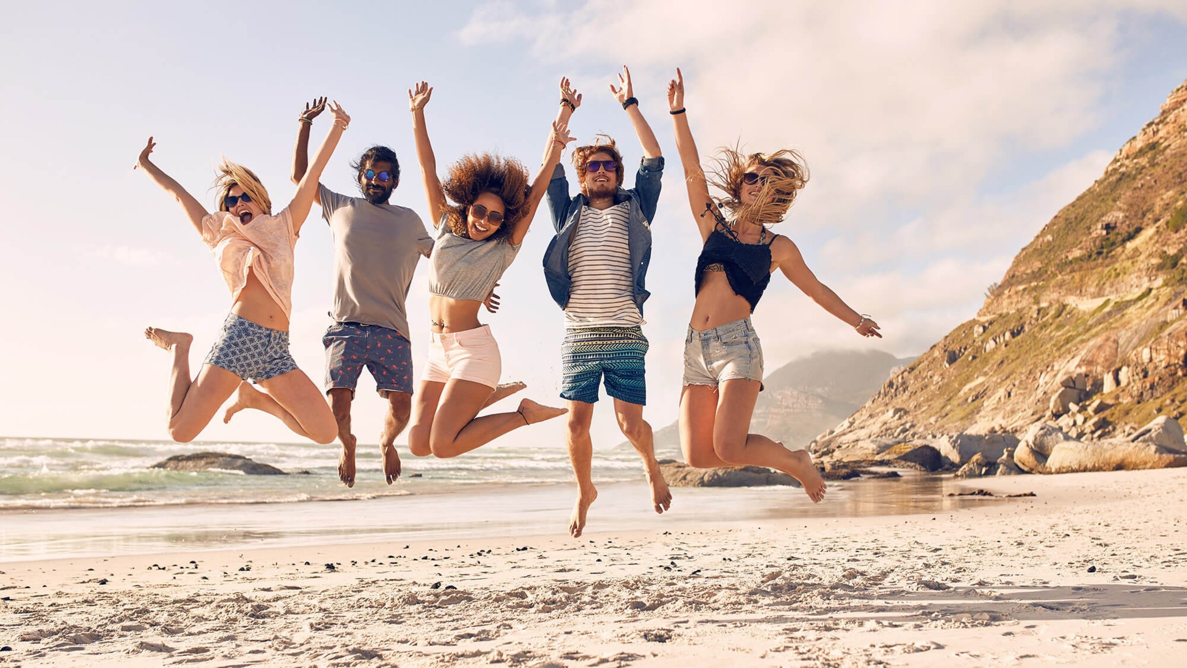 Junge Männer und Frauen am Strand, die vor Freude in die Luft springen
