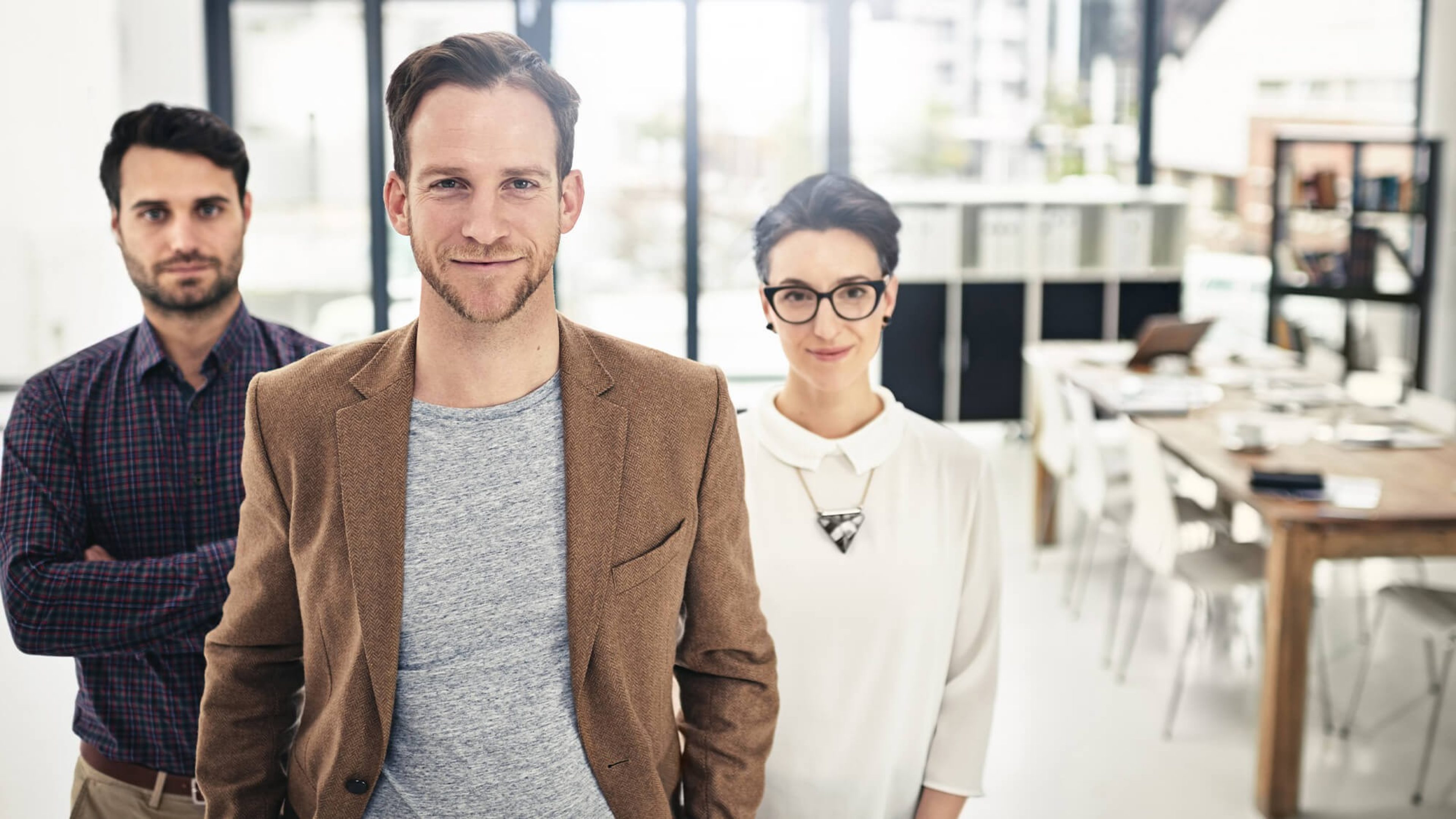 Kolleginnen und Kollegen im Büro blicken selbstbewusst in die Kamera