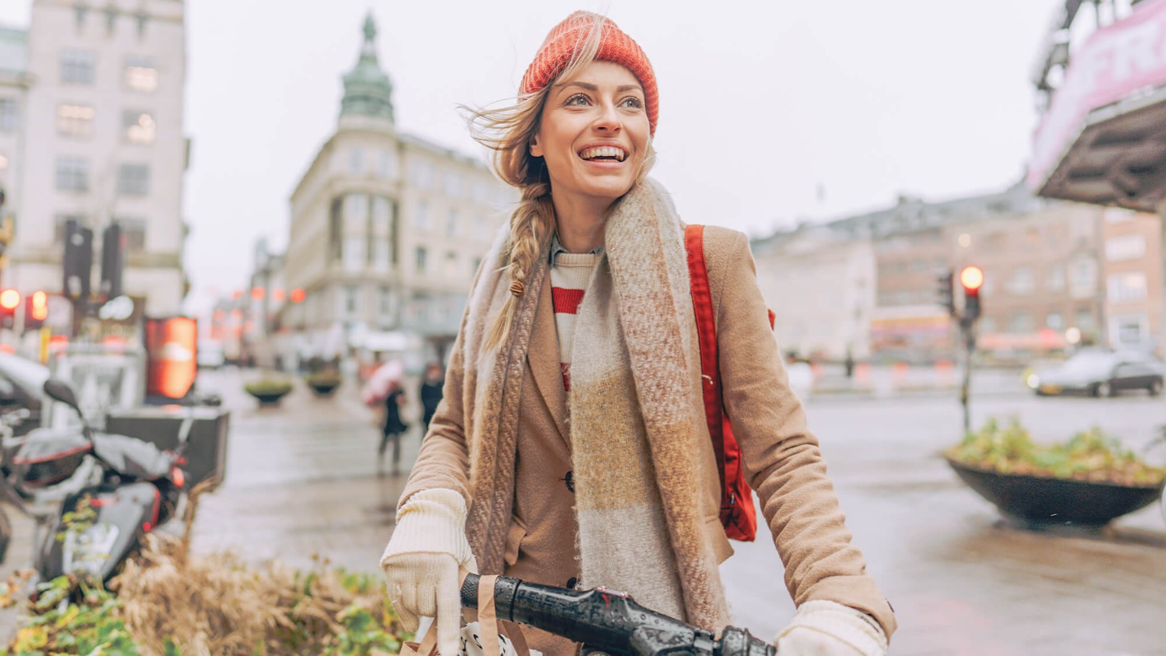 Glücklich Frau mit Mütze, Schal, Mantel und Fahrrad in der Stadt