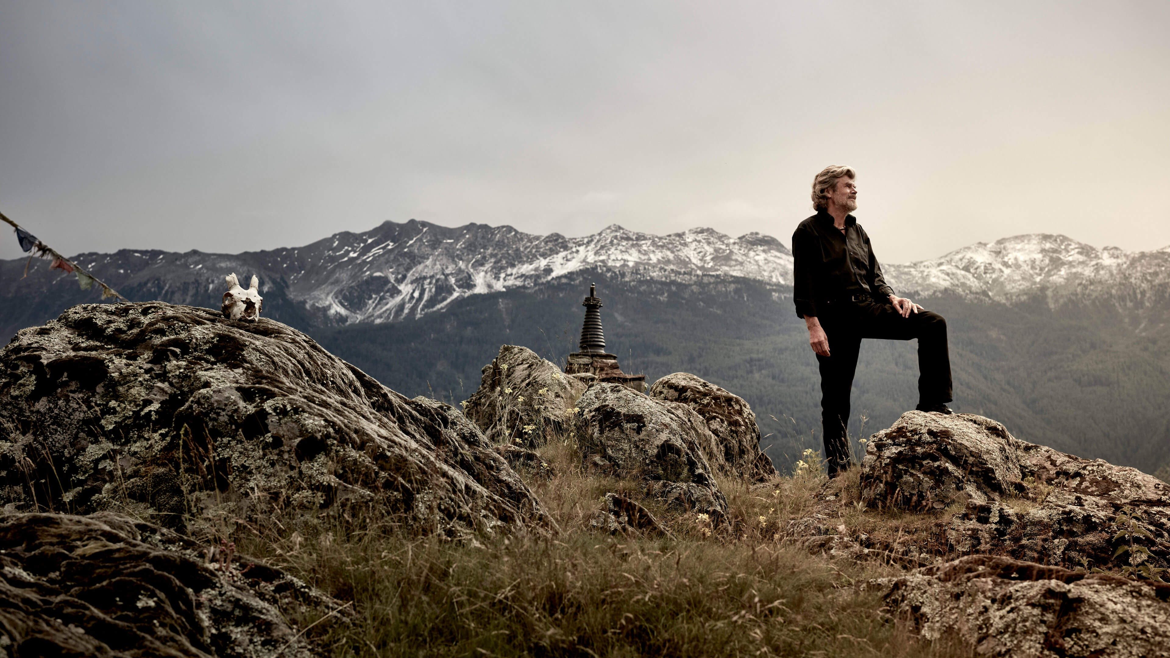 Reinhold Messner auf einem Gipfel und blickt über das Alpenpanorama