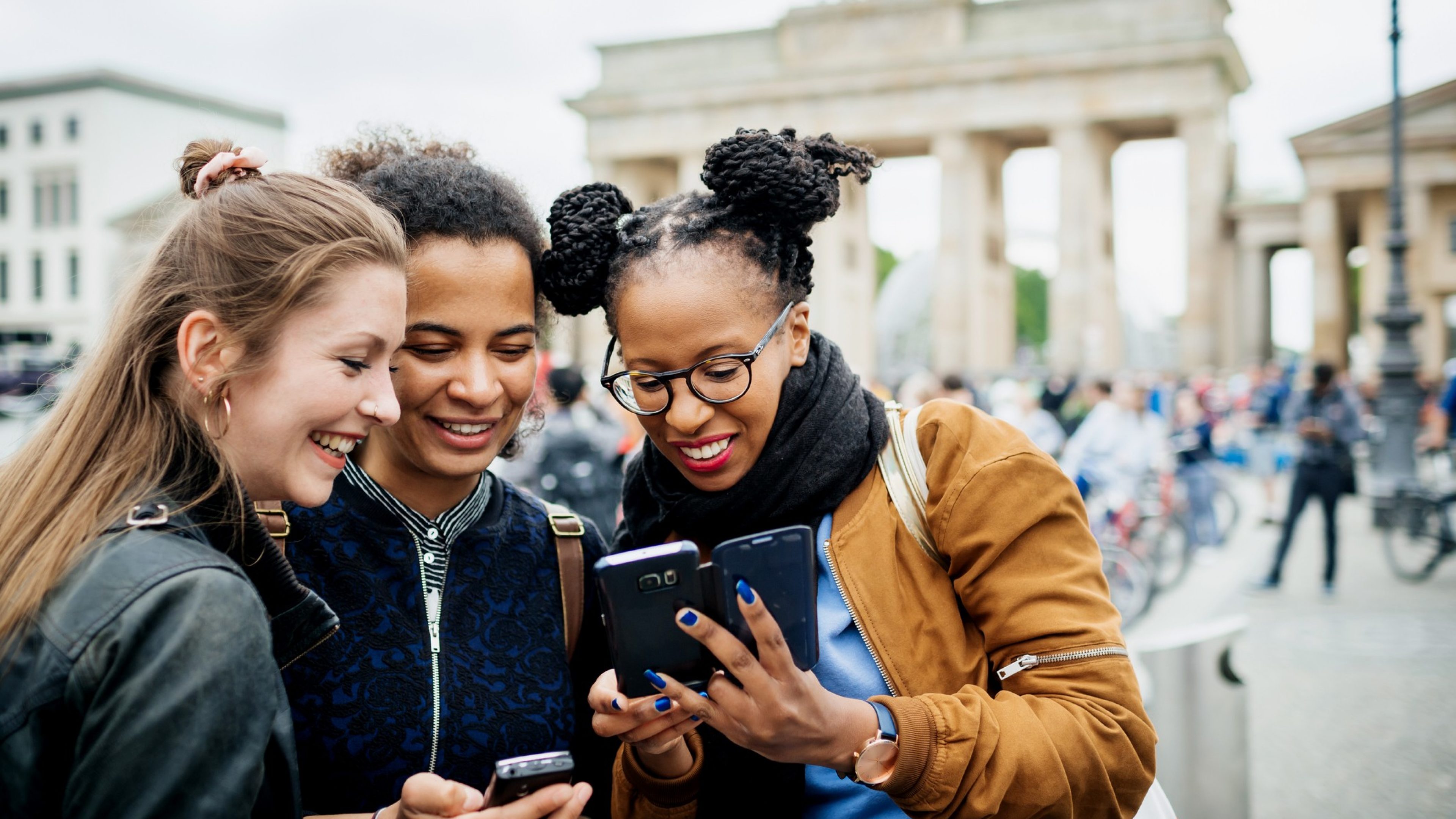 A group of friends travelling together are exploring the local tourist attractions and architecture, they stop for a moment to look over recent photos on their phones.