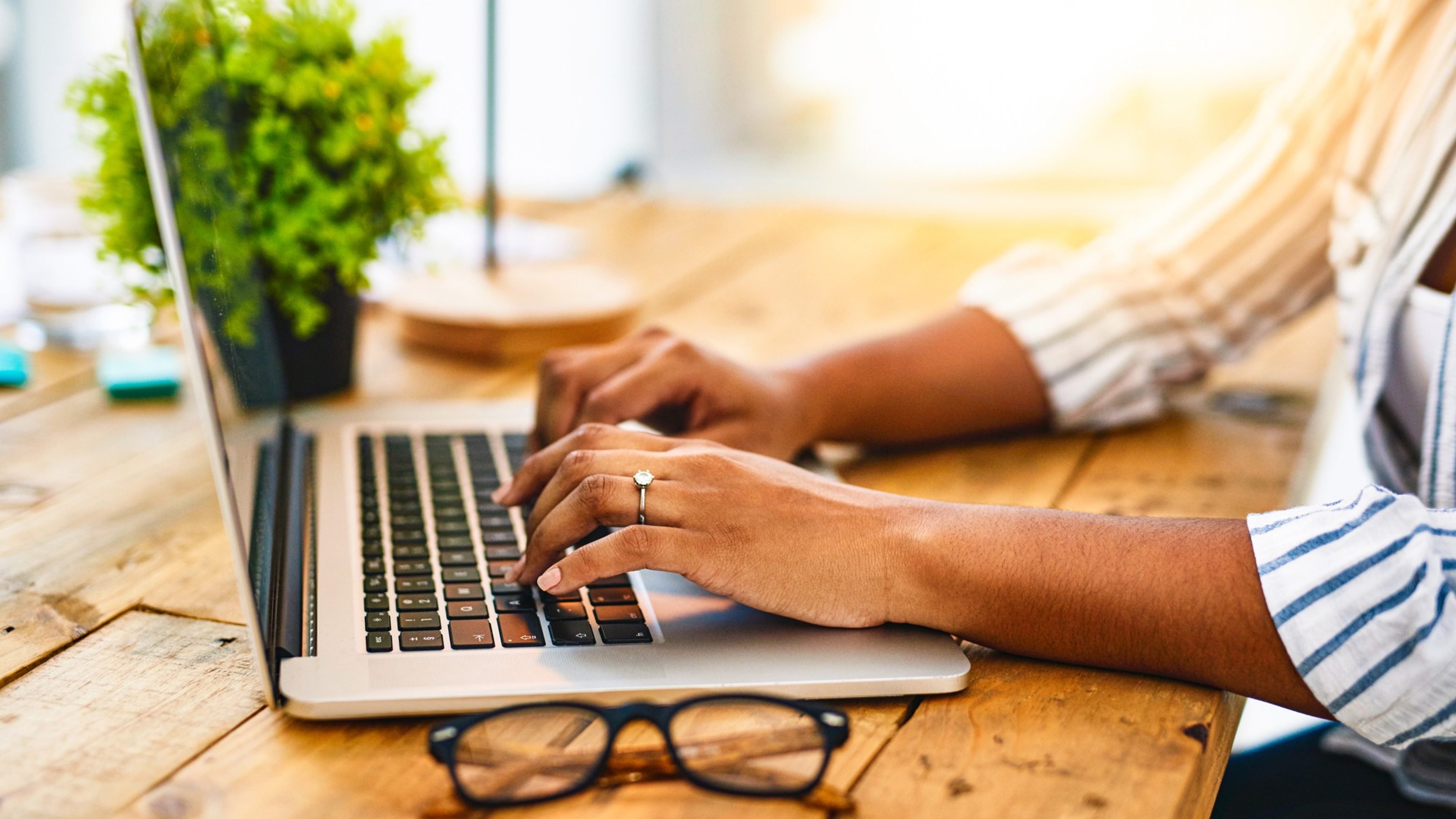 Cropped shot of a woman using her laptop on a wooden table