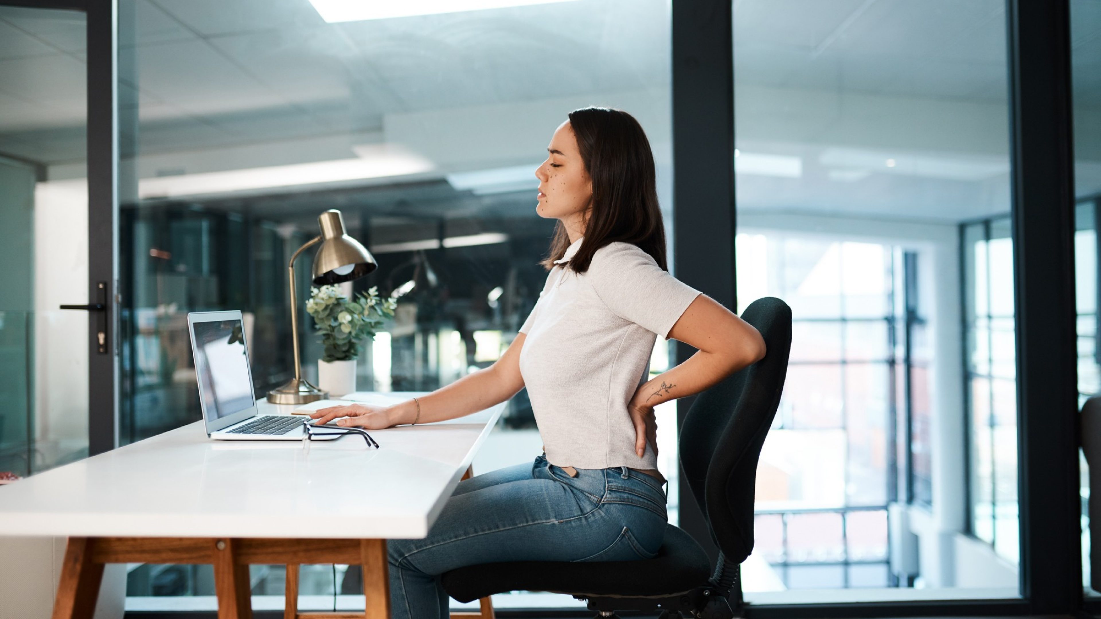 Shot of a young businesswoman experiencing back pain while working in an office