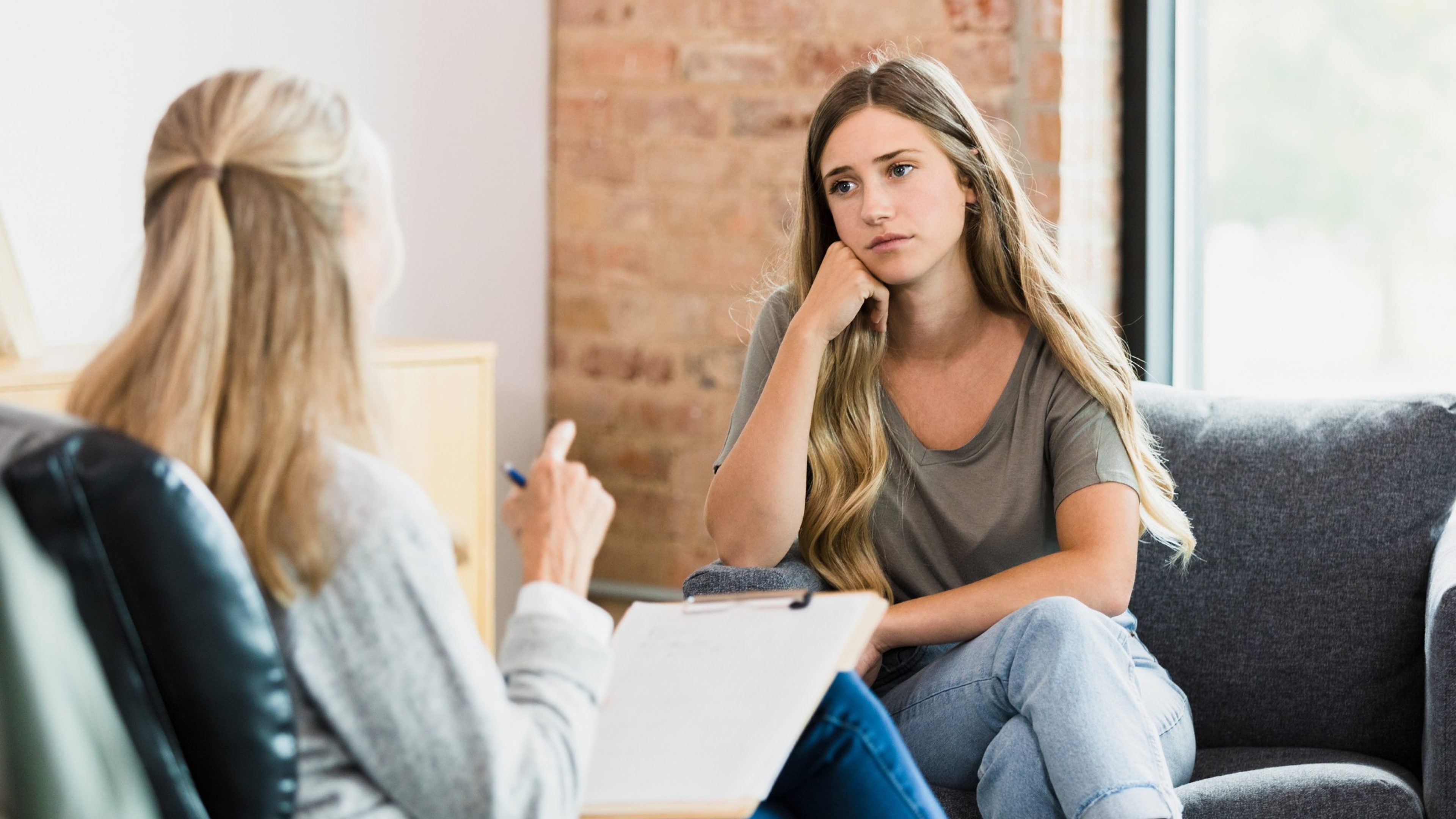 The teenage girl sits hopelessly with her head resting on her hand as she listens to advice from the unrecognizable mature adult female counselor.