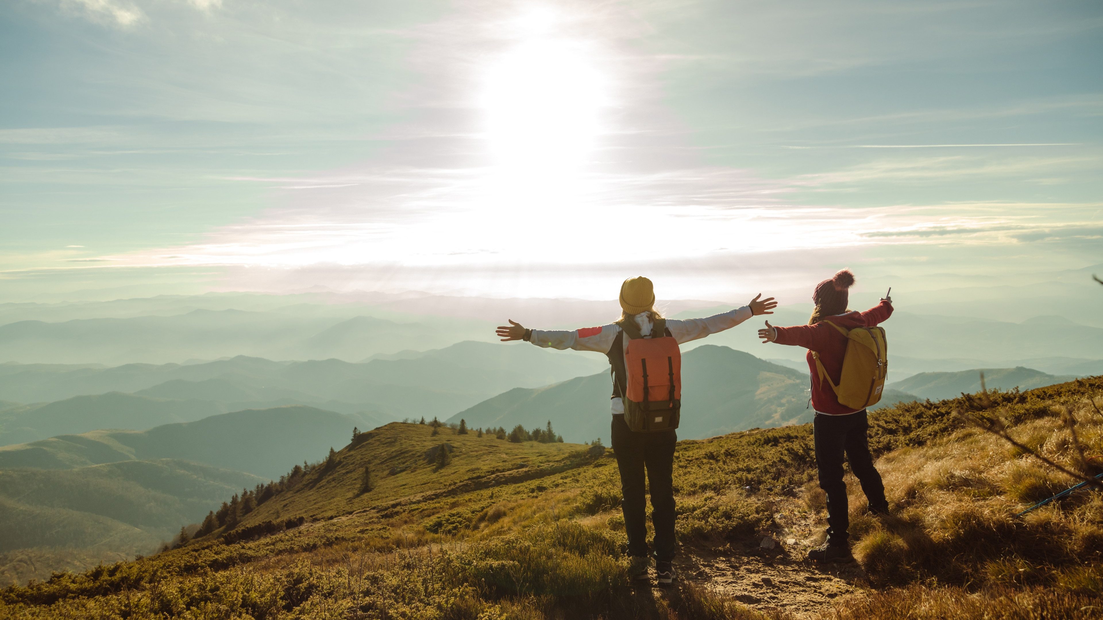 Young female hikers in warm clothes  standing on top of the mountain and looking at the beautiful view
