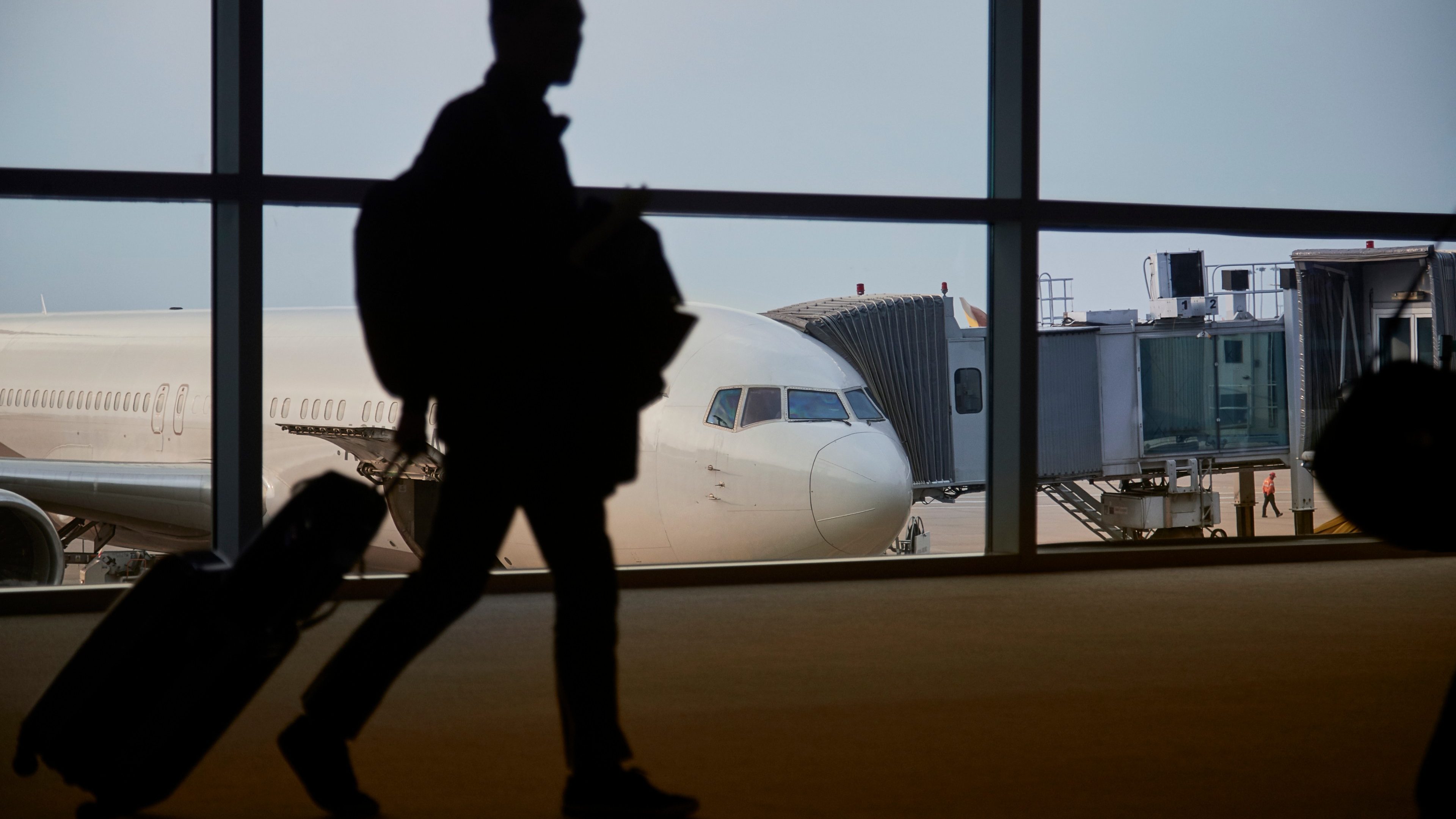 A passenger is in the shadow walking past a commercial aircraft docked to an airport terminal