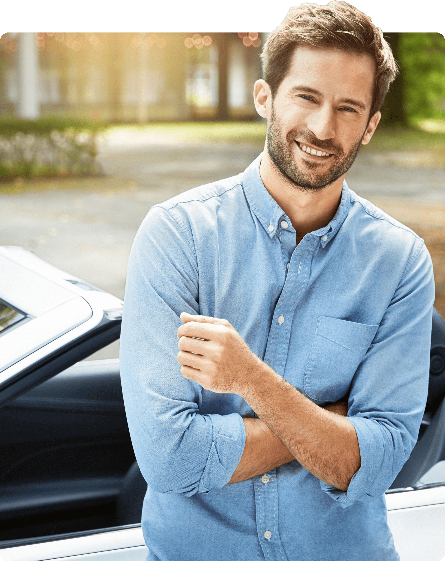 Junger Mann in blauem Hemd mit Blick in die Kamera lehnt an einem Cabrio